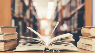 Picture of a book laid open on a table with stacks of books in the backround